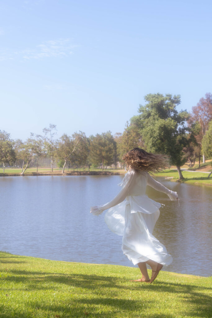 A woman gently pins in white dress, her hands steady and careful. The quiet act reflects resilience and the small, sacred routines of healing.
